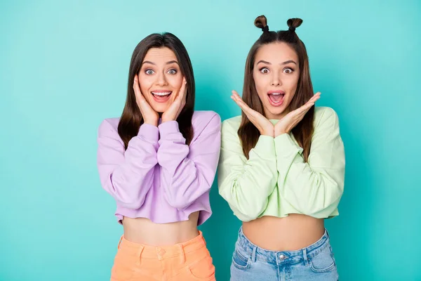 Photo de deux amies assez choquées jeunes filles cool regarder vêtements écouter de bonnes nouvelles bras près des pommettes porter des pulls coupés jupes ventre nu isolé pastel fond de couleur sarcelle — Photo