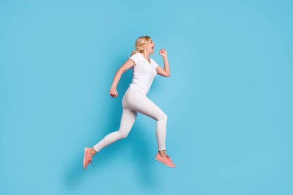 In voller Länge Profilfoto von attraktiven lustigen verrückten Dame springen hohe Laufgeschwindigkeit rauschenden Einkaufszentrum tragen lässige weiße s-Shirt Hose Schuhe isoliert blaue Farbe Hintergrund — Stockfoto