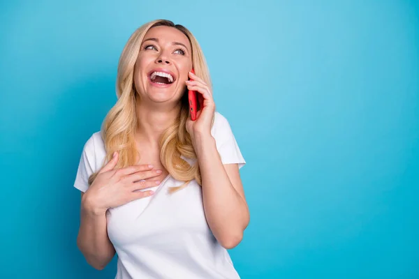 Foto de atractiva mujer ondulada asombrada sostener las manos del teléfono escuchar amigo hablando riendo en voz alta buen humor excitado desgaste casual blanco s-shirt aislado color azul fondo —  Fotos de Stock