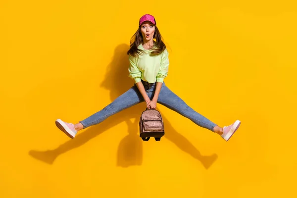 Full size photo of funky energetic attractive lady student good mood hold backpack jump high up wear green cropped sweatshirt jeans shoes cap isolated vivid bright yellow color background — Stock Photo, Image