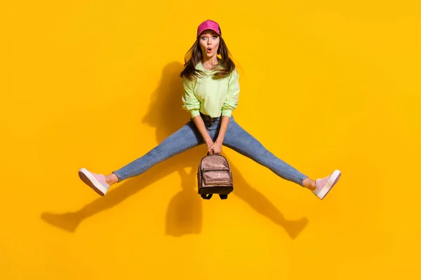 Full size foto van funky energieke aantrekkelijke dame student goed humeur hold rugzak springen hoog dragen groen bijgesneden sweatshirt jeans schoenen cap geïsoleerde levendige felgele kleur achtergrond — Stockfoto