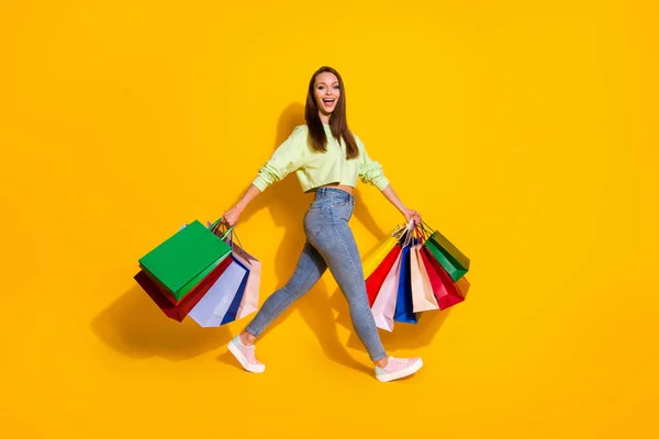 Full length profile side photo of positive excited addicted shopaholic girl go walk hold many bags wear green style stylish trendy outfit isolated yellow color background — Stock Photo, Image