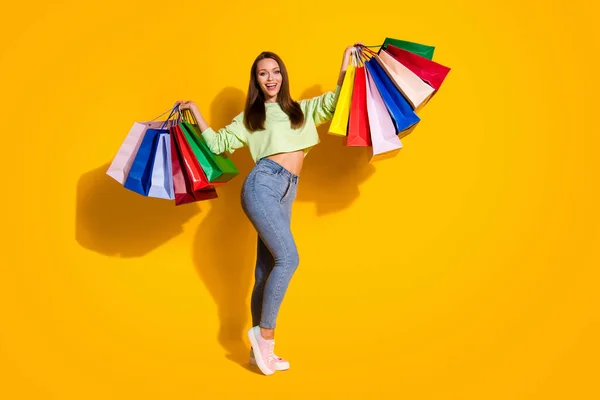 Full length foto di bella signora shopaholic buon umore street look tenere molte borse della spesa indossare verde ritagliato felpa jeans scarpe isolato vivido colore giallo brillante sfondo — Foto Stock