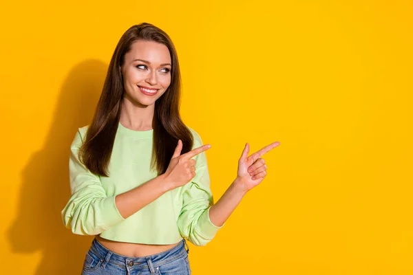 Foto van aantrekkelijke dame goed humeur directe vingers kant lege ruimte tonen nieuwigheid product dragen groen bijgesneden sweatshirt jeans geïsoleerde levendige felgele kleur achtergrond — Stockfoto