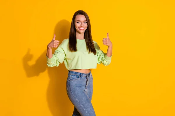 Photo of pretty nice youth lady good positive mood toothy smile raise thumb fingers up approval wear crop green sweter golas belly jeans isolated vivid bright yellow color background — Zdjęcie stockowe