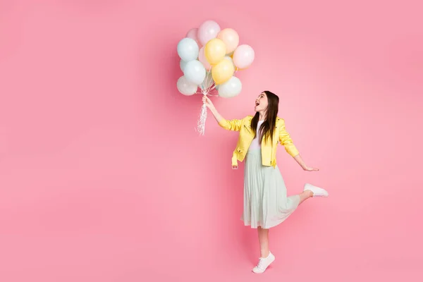 Foto de perfil de cuerpo completo de la señora alegre divertida cogida de la mano muchos globos de aire vuelan por el viento soplando desgaste chaqueta de cuero amarillo verde falda larga zapatos aislados pastel color rosa fondo — Foto de Stock