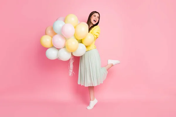 Volledige lengte foto van grappige vrolijke dame houd handen veel luchtballonnen feestelijke gebeurtenis verjaardag partij dragen geel lederen jas groen lange rok geïsoleerde pastel roze kleur achtergrond — Stockfoto