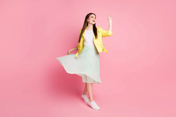 Foto de longitud completa de la señora funky caminar por la calle de buen humor elevar verde largo ondulado brazo de la onda falda ver a los amigos usan chaqueta de cuero amarillo zapatillas de deporte de color rosa pastel aislado fondo —  Fotos de Stock