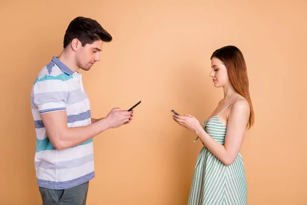 Profiel side photo of married couple man woman use cellphone read social media news feedback wear striped t-shirt jurk rok geïsoleerd over beige kleur achtergrond — Stockfoto