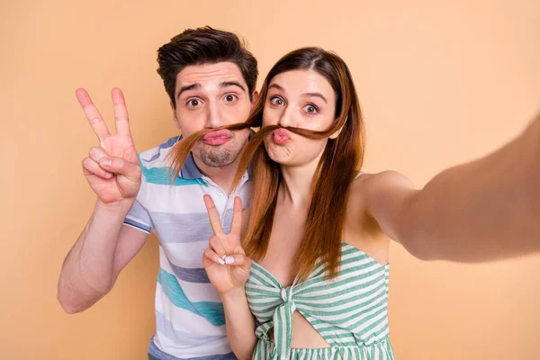 Primeros planos foto de la mujer bonita marido hombre loco pareja infantil pasar tiempo tomar selfies mostrar v-signo de hacer falsos bigote rizos usar ropa casual aislado color beige fondo —  Fotos de Stock