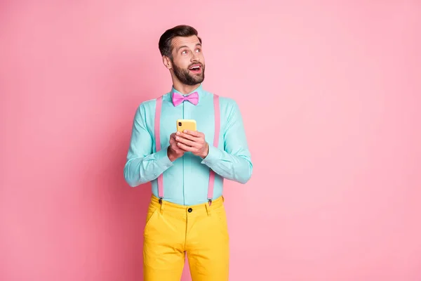 Photo of handsome guy trend clothes look side empty space novelty banner browsing telephone hands blogger wear shirt suspenders bow tie trousers isolated pastel pink color background — Stock Photo, Image