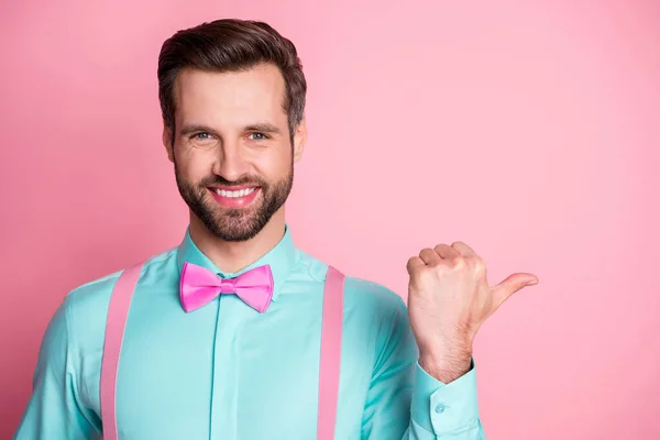 Photo of handsome guy trend clothes direct thumb finger side empty space toothy smile showing novelty banner wear shirt suspenders bow tie isolated pastel pink color background — Stock Photo, Image