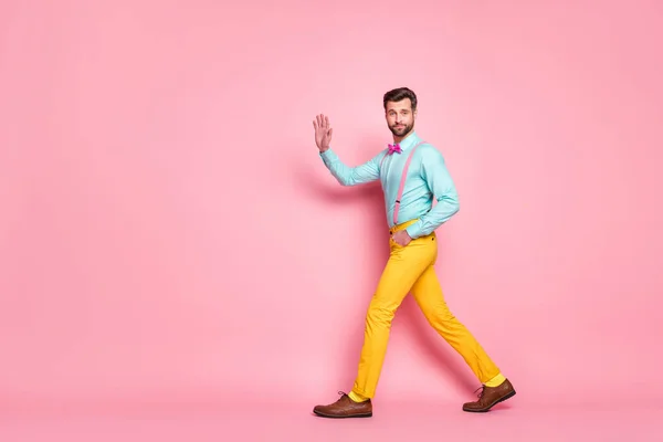 Pełna długość profil zdjęcie przystojny facet trend wygląd spacer spotkanie czerwony dywan celebryci machanie ręka nosić koszulka szelki muszka żółty spodnie obuwie odizolowany pastelowy różowy kolor tło — Zdjęcie stockowe