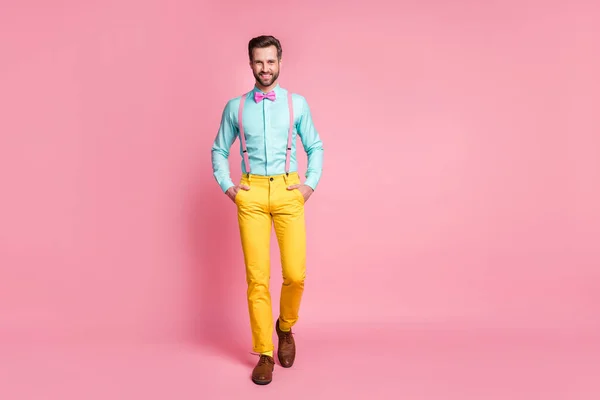 Full size photo of handsome guy trend clothes beaming smile walking office meeting wear teal shirt suspenders bow tie yellow trousers boots socks isolated pastel pink color background — Stock Photo, Image