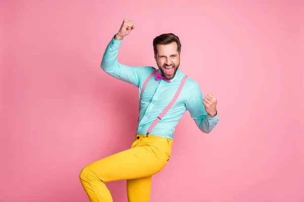 Фото красивый взволнованный мачо парень модная одежда зубастые сияющие улыбки поднять кулаки вверх руки ура носить подтяжки рубашки бирюзовый галстук желтые брюки изолированные пастельно-розовый цвет фона — стоковое фото