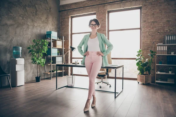 Full body photo of positive real estate agent δικηγόρος κορίτσι σταθεί στο σύγχρονο γραφείο βάλει τα χέρια μέση φορούν πράσινο σακάκι σακάκι σακάκι ροζ παντελόνι παντελόνι ψηλά τακούνια — Φωτογραφία Αρχείου