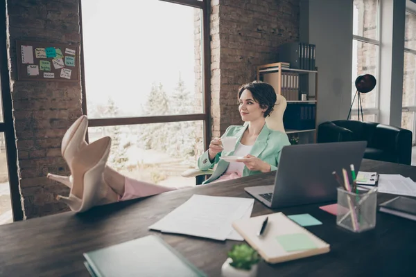 Profile photo of beautiful charming business lady hold coffee mug cup resting house remote distance work look window legs on table notebook legs table sit big chair office indoors