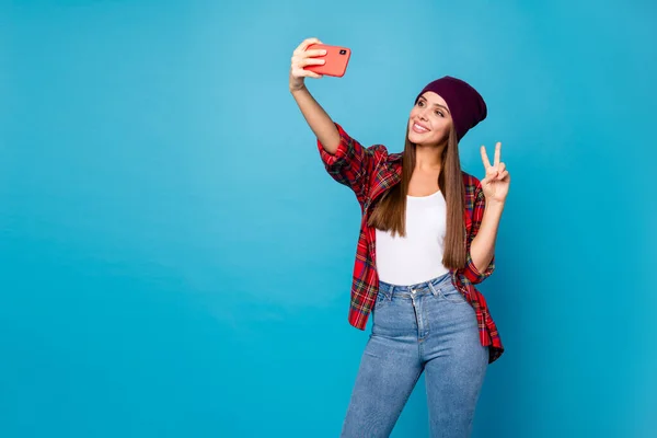 Foto di bella signora tenere telefono blogger fare selfie mostrando v-segno simbolo strada guardare nuovo ritratto indossare casual cappello plaid camicia jeans isolato blu colore sfondo — Foto Stock