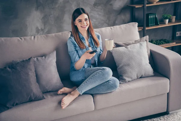 Fotografie pozitivní veselá dívka sedět pohodlné divan hodinky film držet dálkové ovládání vypínače kanály v obývacím pokoji bytový dům uvnitř — Stock fotografie