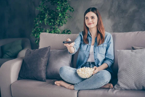 Portret van positief mooi meisje zitten divan benen gekruist bekijk interessante film wissel kanalen eten popcorn blootsvoets in huis binnen — Stockfoto