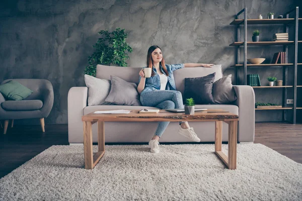 Foto de longitud completa de bastante agradable chica franca sentarse cómodo diván mirada disfrutar de quedarse en casa cuarentena fin de semana celebrar café taza de capuchino en la casa habitación interior — Foto de Stock