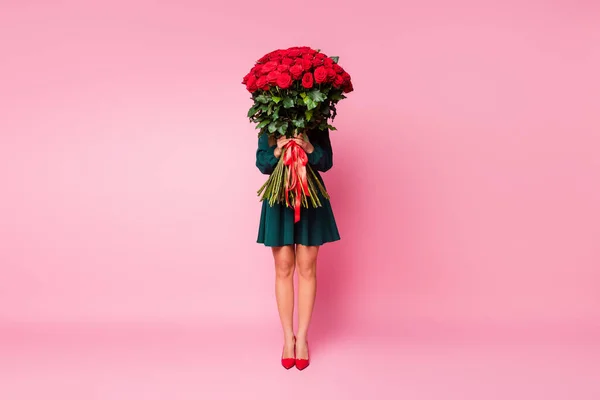 Ganzes Foto von charmanten eleganten Dame halten Arme große Rosen Strauß verstecken Gesicht schüchterne Person tragen kurze grüne Kleid rot High-Heels isoliert pastellrosa Farbe Hintergrund — Stockfoto