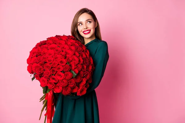 Foto de atractiva dama rojo brillante lápiz labial celebrar grandes rosas ramo novio presente mirar lado vacío espacio interesado usar vestido verde aislado pastel rosa color fondo — Foto de Stock