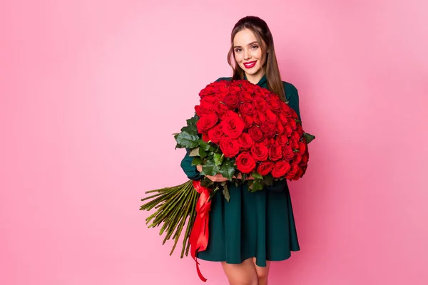 かわいい魅力的なシックな女性の写真を保持大規模な赤い長いバラの花束秘密の愛好家のボーイフレンド誕生日の驚きは緑のミニドレス孤立パステルピンク色の背景を身に着けている — ストック写真