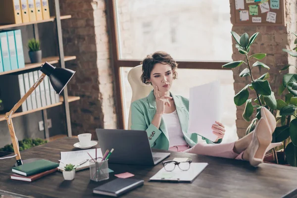 Foto di attraente business boss signora notebook tavolo distanza casa lavoro remoto tenere i documenti leggere contratto gambe interessate sul tavolo fiducioso capo sedersi sedia moderno ufficio interno al chiuso — Foto Stock