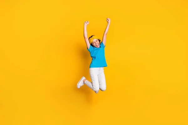Full length photo of crazy little lady jump high up good mood celebrate competition winning raise fists wear casual blue t-shirt headband trousers shoes isolated yellow color background — Stock Photo, Image