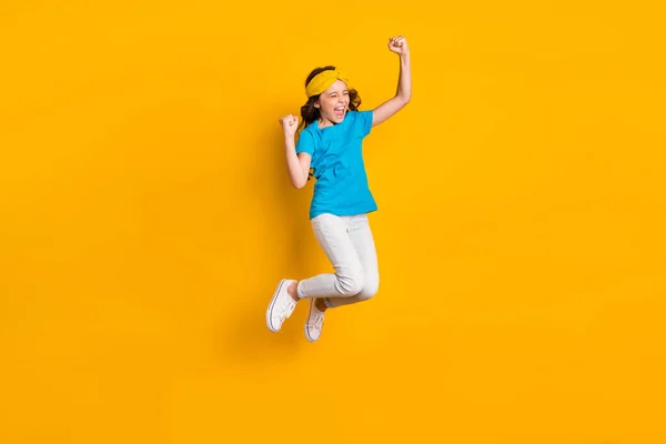 Фотографія повного тіла смішної божевільної маленької леді, що стрибає з високим гарним настроєм, святкування змагань виграють підняти кулаки, одягнені в казуальну синю футболку взуття для штанів ізольовані жовтого кольору — стокове фото