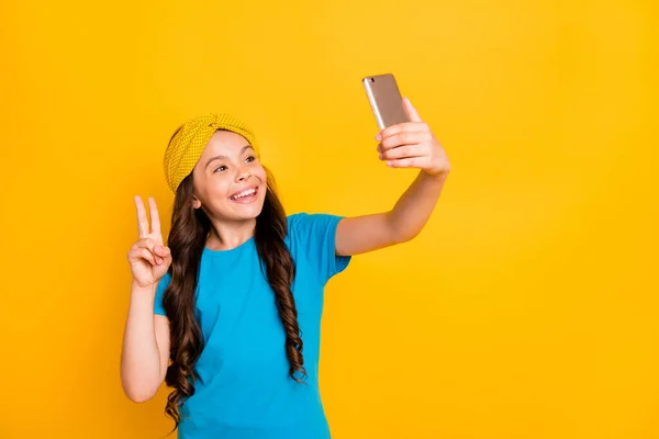 Foto de divertida señorita mantener el teléfono cuarentena tiempo quedarse en casa hablar skype compañeros de clase mostrar v-signo decir hola señorita amigos usar casual azul camiseta diadema aislado color amarillo fondo — Foto de Stock