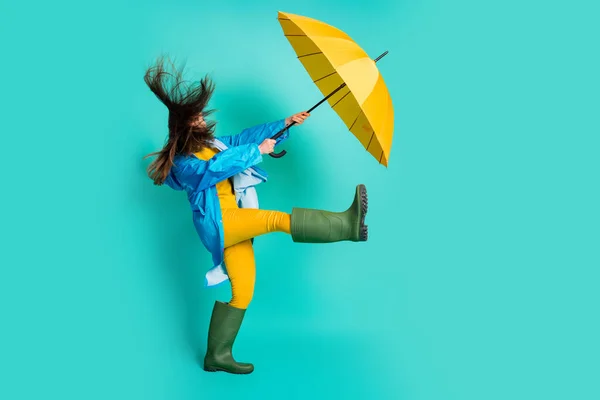 Full length profile photo of shocked lady stormy rainy weather walk street hold umbrella catch strong wind blew away wear raincoat sweater pants gumboots isolated teal color background — Stock Photo, Image