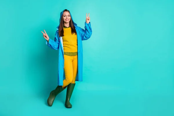 Foto de longitud completa de la atractiva dama alegre encantador tiempo lluvioso calle paseo espectáculo v-signo símbolos desgaste traje casual impermeable capucha botas de goma aislado color verde azulado fondo —  Fotos de Stock