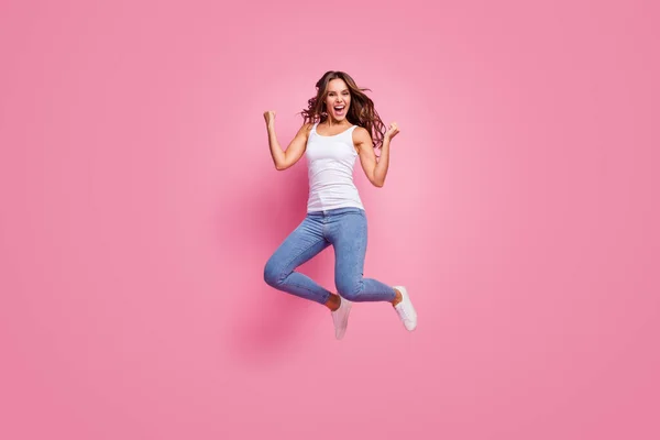 Фотографія повного тіла божевільної збудженої леді стрибає з високим настроєм підняти кулаки святкувати успіх вигравайте одяг білий повсякденні джинси взуття ізольовані рожевий колір фону — стокове фото