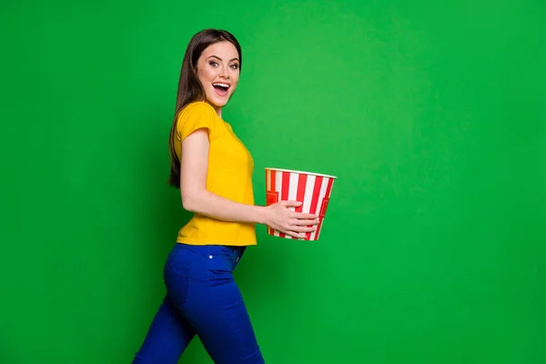 Profile side photo of positive cheerful girl hear her favorite series start hold big pop corn box go walk watch living room wear stylish trousers isolated over bright color background — Stock Photo, Image