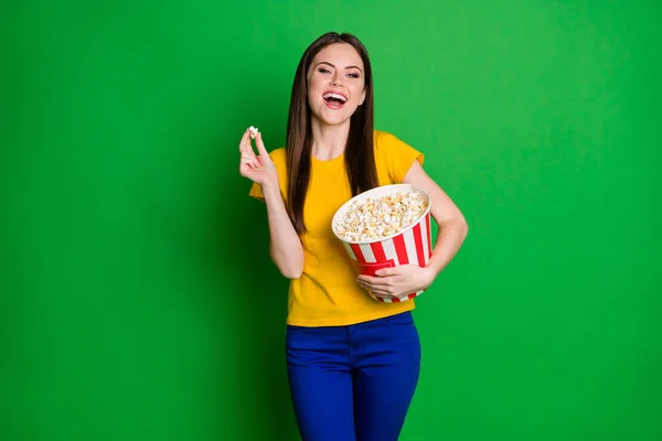 Porträt von positiven fröhlichen Mädchen halten große Popcorn-Box beobachten lustige Serie lachen tragen gelbe Hosen isoliert über Glanz Farbe Hintergrund — Stockfoto