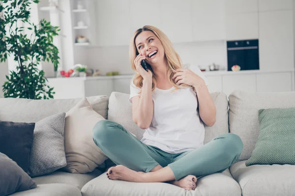 Foto de domestico alegre hermosa rubia dama sentarse sofá sostener teléfono charlando amigos parientes familiares cuarentena quedarse en casa buen humor piernas cruzadas sala de estar en el interior — Foto de Stock