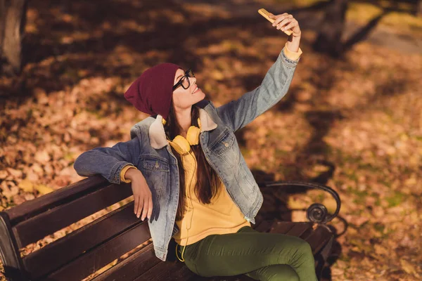 그녀의 매력적 이고 쾌활 한 아가씨가 벤치노란 나뭇잎 햇볕이 잘 드는 날 야외에서 셀카를 공짜로 쉬게 하는 모습 — 스톡 사진