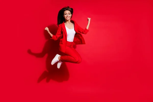 Volledige lengte foto van aantrekkelijke dame werknemer het hebben van plezier springen hoog op goed humeur vieren startup succes dragen blazer pak broek schoeisel geïsoleerd helder rood kleur achtergrond — Stockfoto