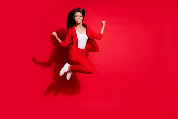 Full length photo of attractive lady worker having fun jumping high up good mood celebrate startup success wear blazer suit pants footwear isolated bright red color background