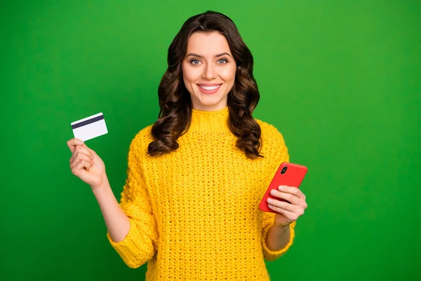 Πορτρέτο της θετικής χαρούμενο κορίτσι χρησιμοποιούν έξυπνο τηλέφωνο απολαμβάνουν εύκολη online πληρωμή με χρεωστική κάρτα φορούν στυλ κομψό μοντέρνο κίτρινο πουλόβερ πουλόβερ πουλόβερ που απομονώνονται πάνω από φωτεινό χρώμα λάμψη φόντο — Φωτογραφία Αρχείου