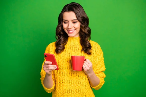 Portret van positieve vrolijke meisje rust ontspannen hold mok drank cappuccino gebruik smart phone delen repost social media nieuws dragen gele trui winter geïsoleerd over felle glans kleur achtergrond — Stockfoto