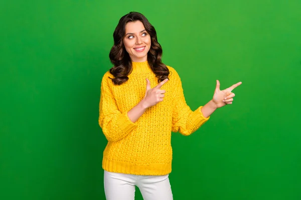 Foto de señora bonita cogida de la mano dirigiendo los dedos mirada espacio vacío asesoría oferta novedad desgaste de punto amarillo jersey pantalones blancos aislados de color verde brillante fondo —  Fotos de Stock