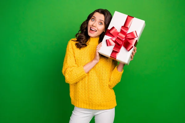 Foto de la señora bonita divertida celebrar gran caja de papel arco rojo cerca de la cabeza cumpleaños fiesta evento regalo desgaste punto suéter amarillo pantalones blancos aislados vibrante color verde fondo —  Fotos de Stock