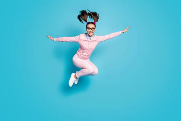 Full size foto van vrolijke middelbare school student meisje springen hold hand stel je voor dat ze vliegen vliegtuig academische les dragen roze kleding sneakers geïsoleerd over blauwe kleur achtergrond — Stockfoto