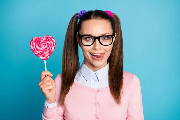 Portrait of positive funny funky girl high school student hold heart shape lollipop want eat lick lips tongue wear good look clothes isolated over blue color background — Stock Photo, Image