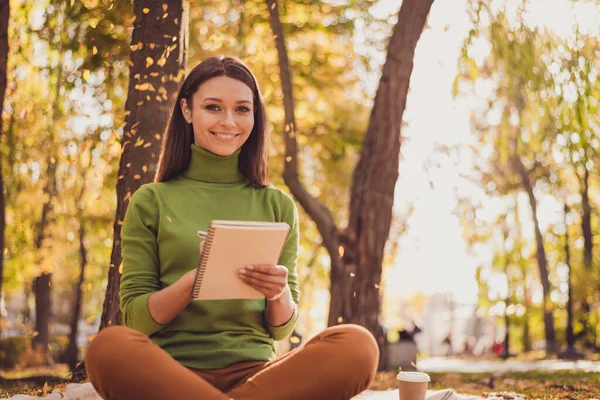 Foto di carino bella signora sedersi coperta tenere penna copybook scrittura fare i compiti a casa sorridente luogo tranquillo autunno parco aspettare amico preparare insieme indossare verde dolcevita pantaloni arancioni all'aperto — Foto Stock