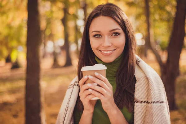 귀여운 아가씨가 커피 잔을 들고 기다리고 있는 사진입니다. 포장 된 격자무늬 담요로 웃으며 시원 한 날씨에 시원하게 야외에서 녹색 터틀넥 오렌지 바지를 입고 자유 시간을 보냅니다. — 스톡 사진