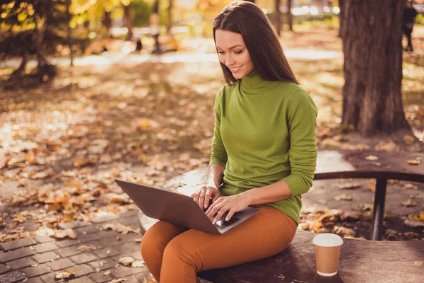 Photo of pretty cute lady sit bench autumn park hold laptop drink kawa zdalna praca copywriting wziąć zamówienie projekt sms odpowiedzi nosić zielony golf pomarańczowe spodnie na zewnątrz — Zdjęcie stockowe